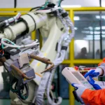 Two technicians work with a robotic arm. Manufacturers are implementing strategies to get workers on board with working in tandem with autonomous tools and technologies. eyesfoto via Getty Images