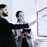 Two business people looking at a screen with data analytics.