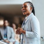 woman in blazer speaking in front of a group